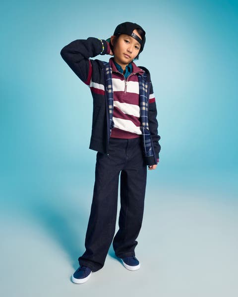 A child wearing a layered rugby stripe polo, plaid shirt, and navy wide-leg pants.