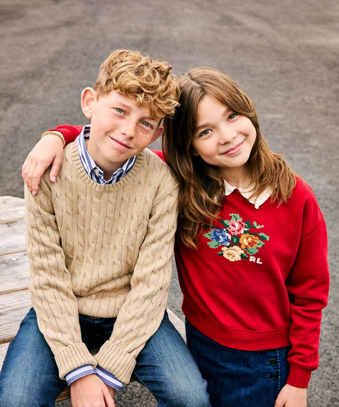 Two kids, a boy and a girl, sit together on a picnic table wearing cozy knit and cross-stitch sweaters.