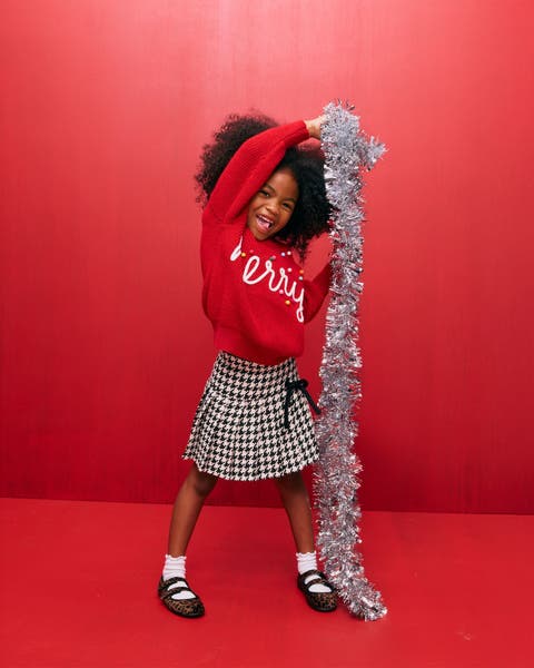 A girl in a holiday sweater holding tinsel garland.