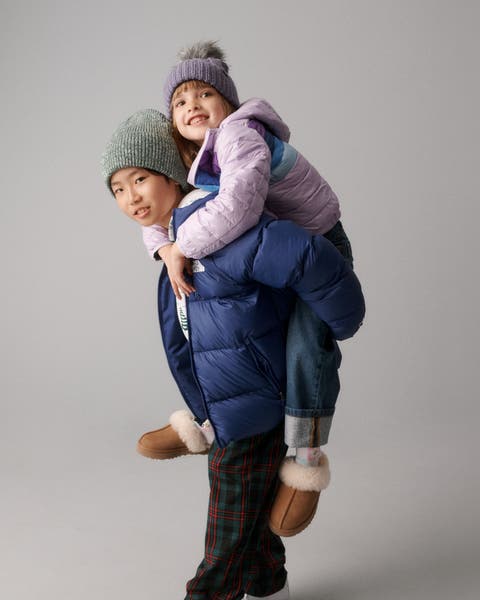Two kids wearing puffers, jeans, and beanies.