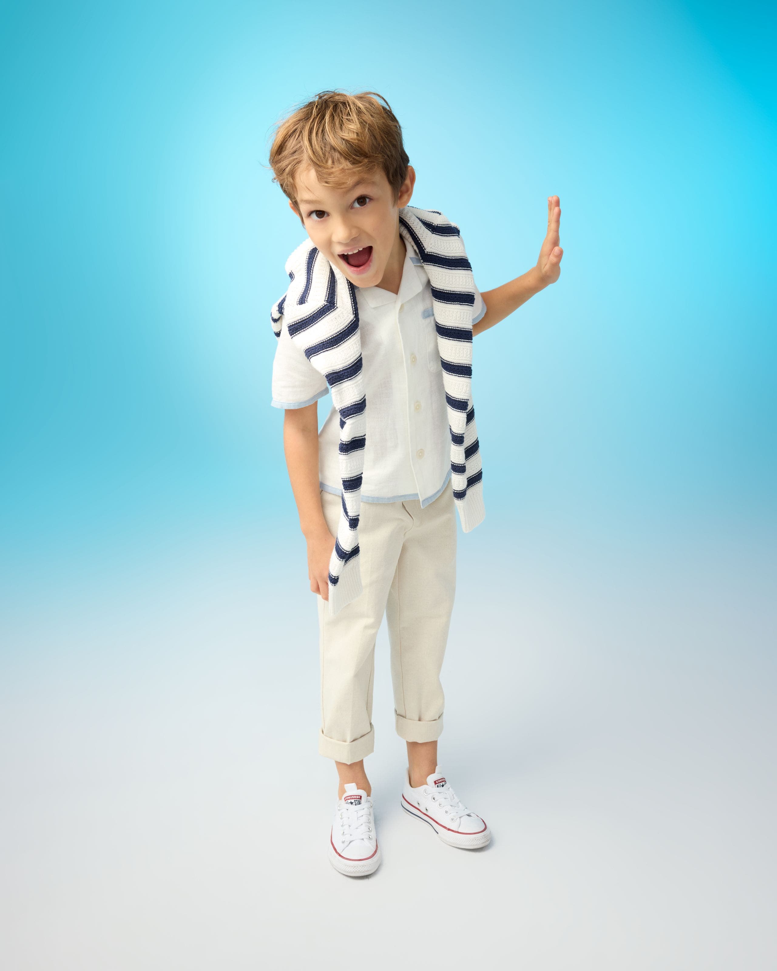 A child wearing a blue and white striped sweater over a white shirt with pants and sneakers.