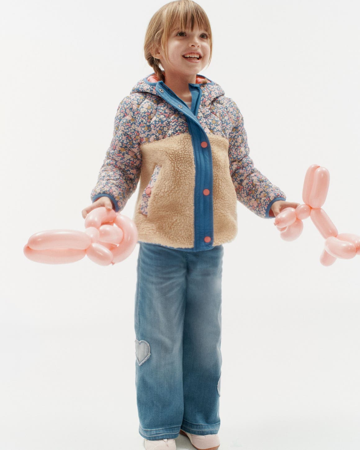 A girl in a mixed-media jacket and heart-embroidered jeans holding balloon animals.