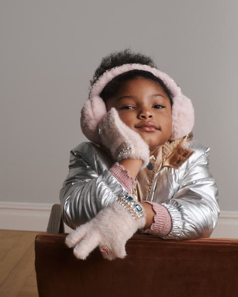 A girl wearing earmuffs, gloves and a silver jacket.