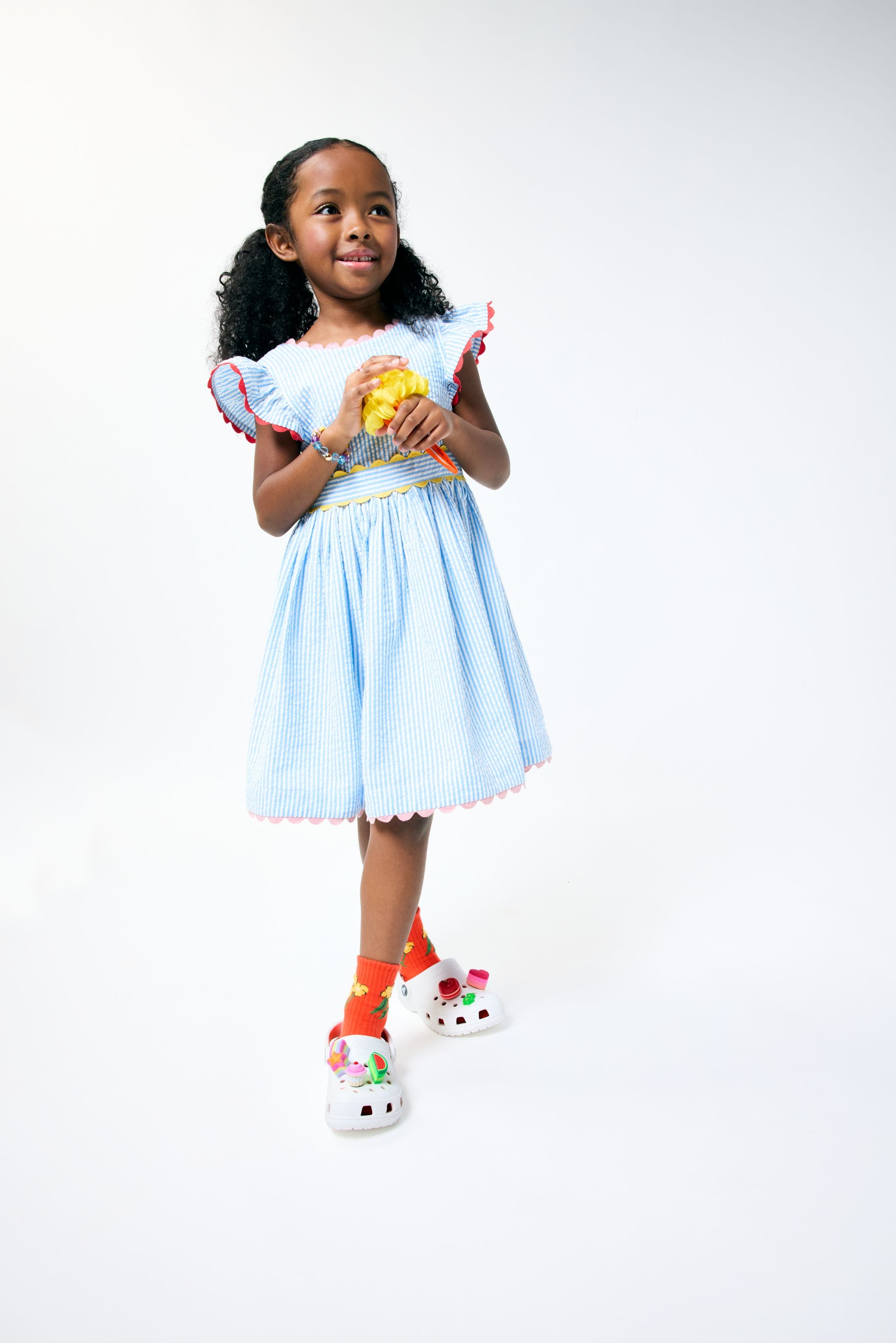 A little girl wearing a light blue dress with scalloped trim from Mini Boden.