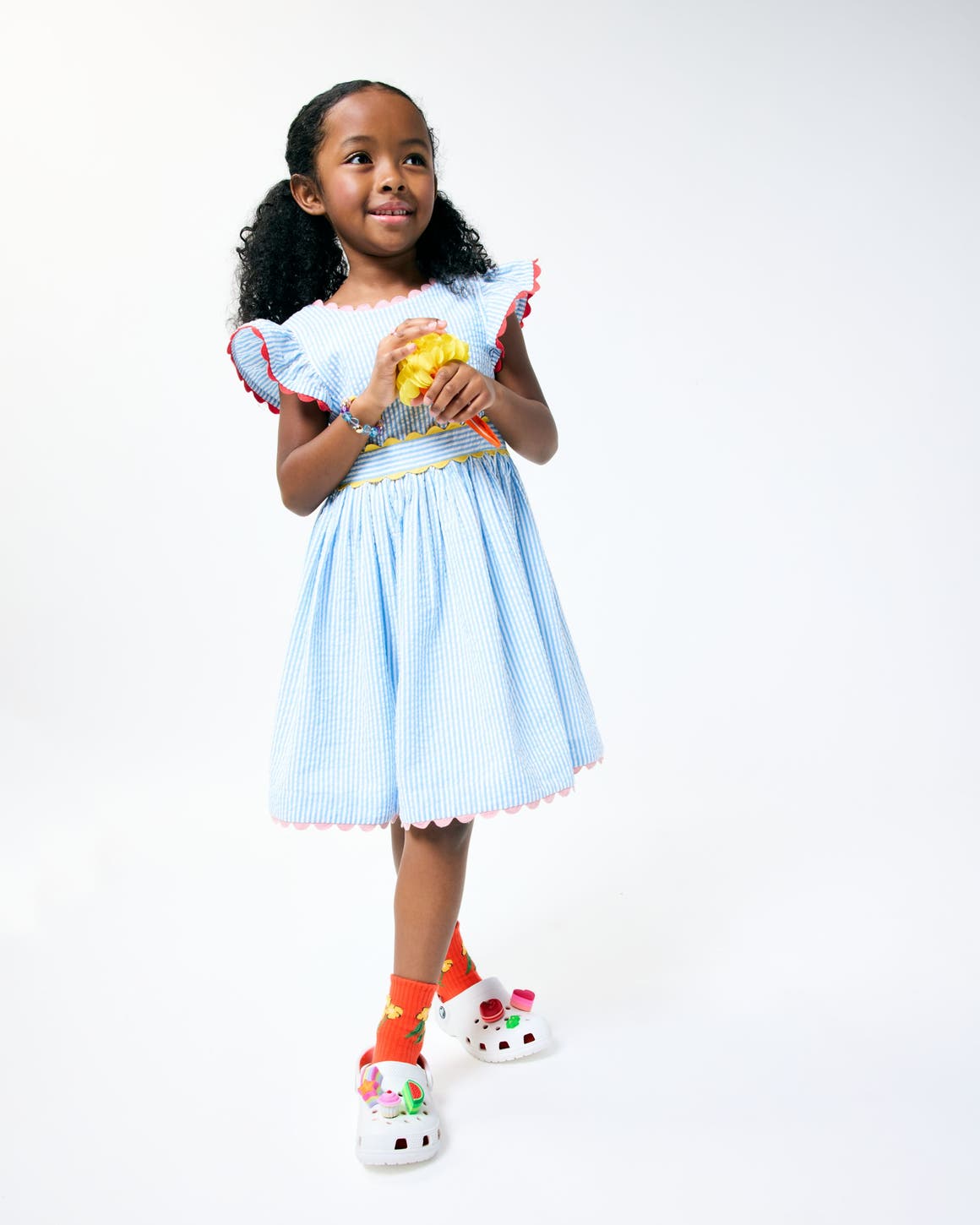 A little girl wearing a light blue dress with scalloped trim from Mini Boden.