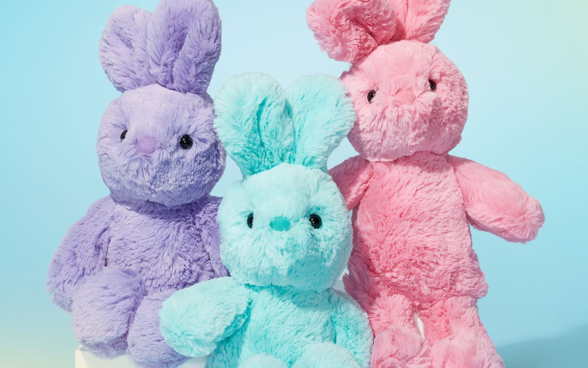 Three bunny-shaped stuffed animals in purple, blue and pink.