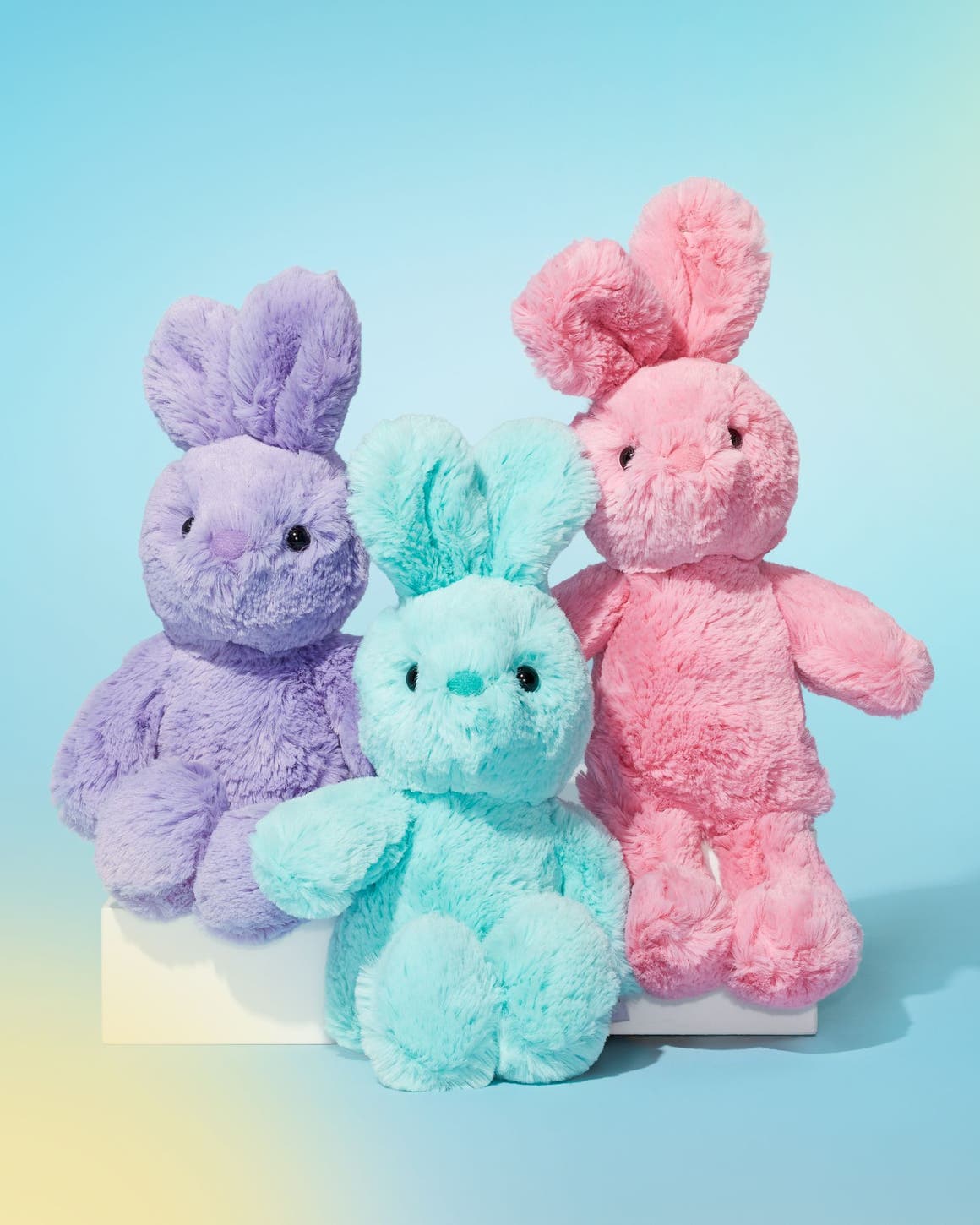 Three bunny-shaped stuffed animals in purple, blue and pink.