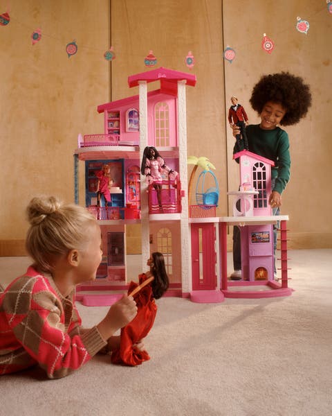 Two children playing with a Barbie house.