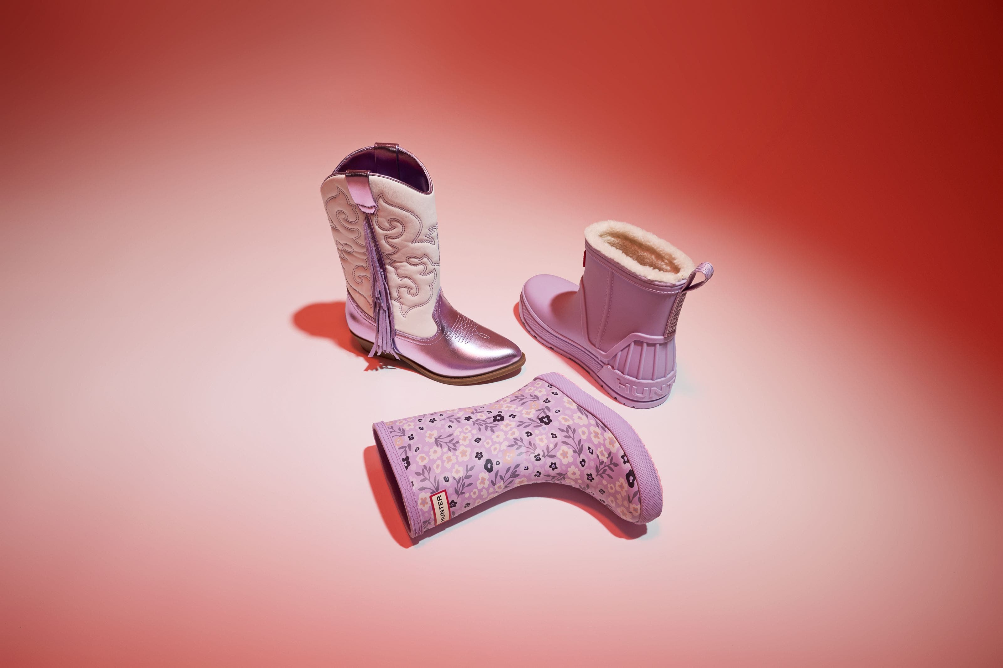 Lavender western and rain boots, one floral and one fleece-lined, on pink.