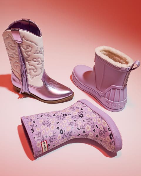 Three children's boots in pink and lavender including a western cowboy boot, a Hunter rain boot, and a Hunter shearling-lined boot.