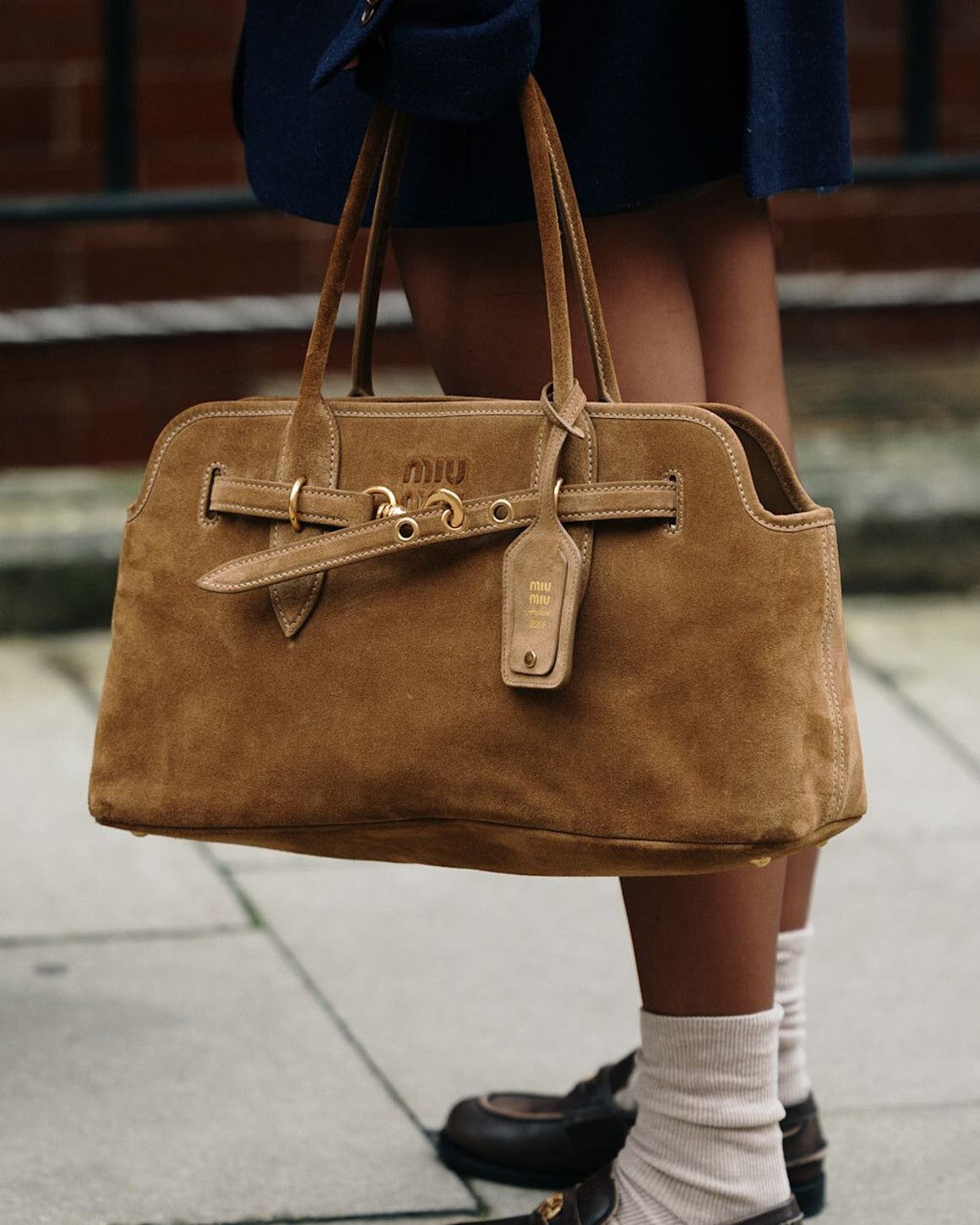 Person carrying a suede tote bag at London Fashion Week.