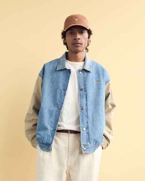 A man wearing a denim-front varsity jacket.