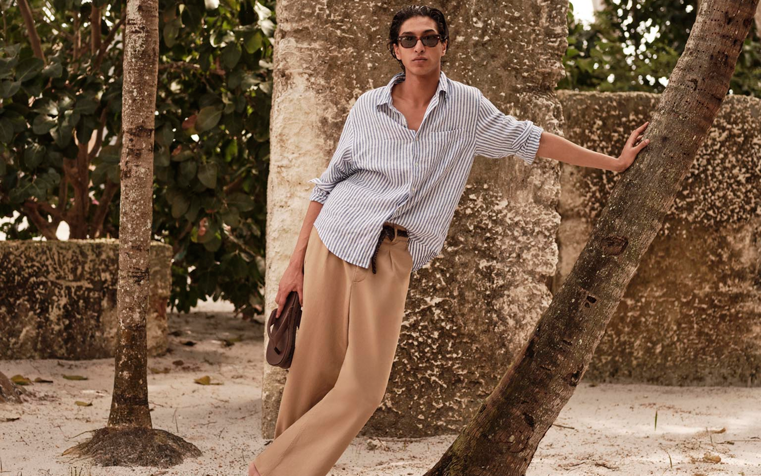 A man wearing a striped button down and linen pants. 