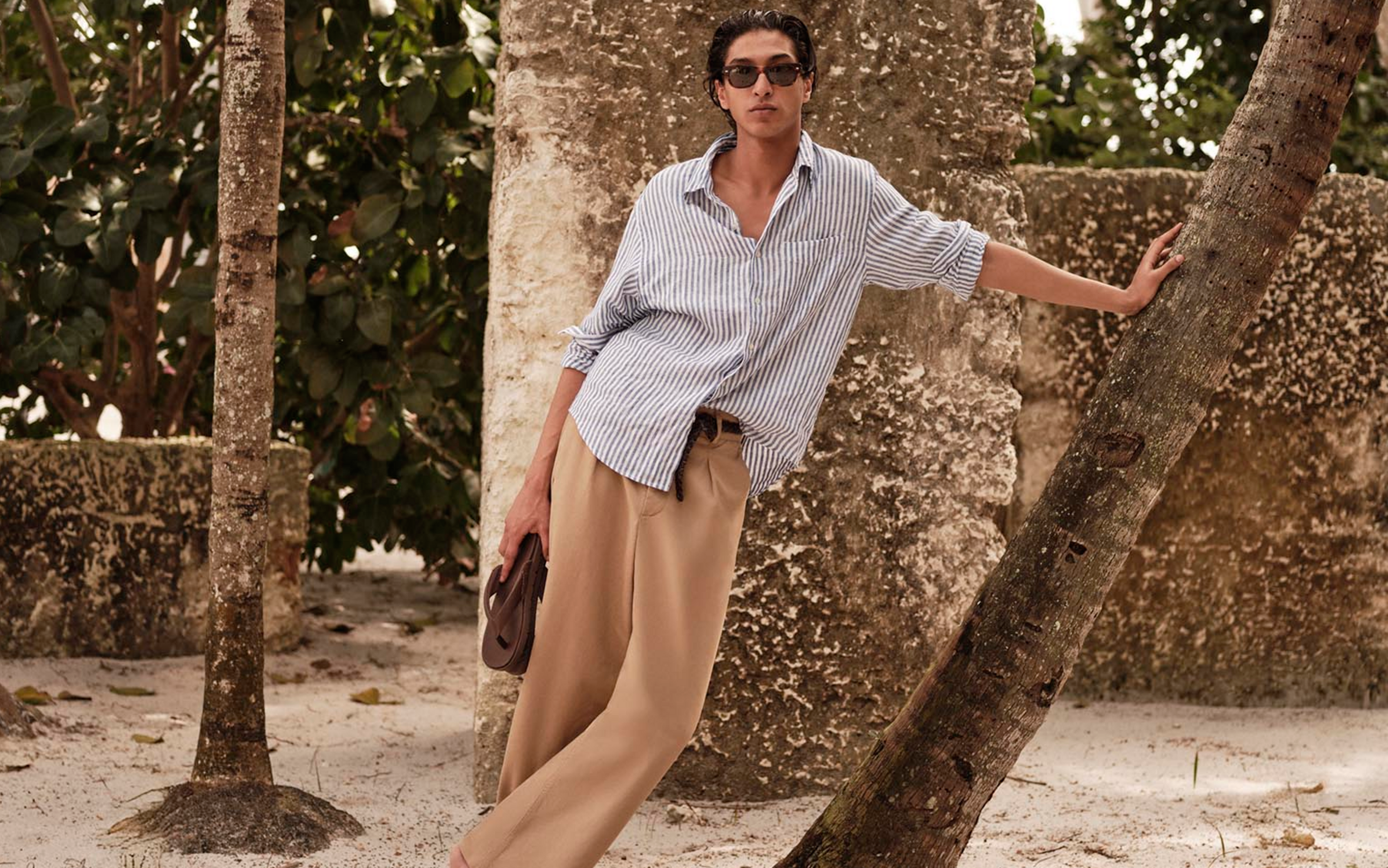 A man wearing a striped button down and linen pants.