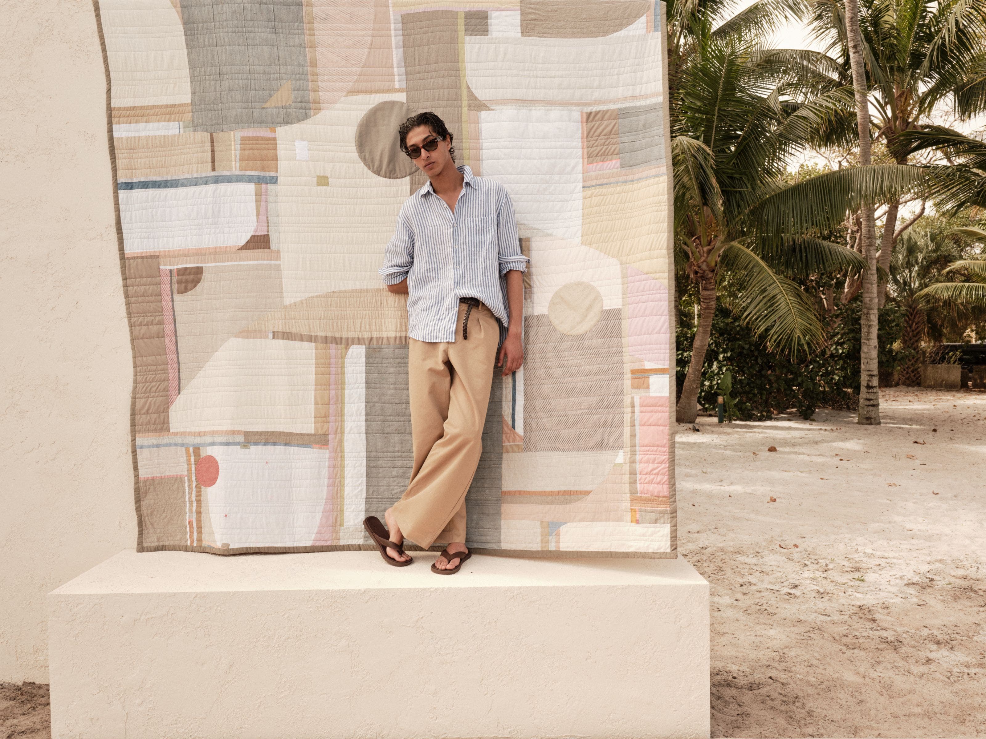 A man wearing a striped linen shirt, relaxed tan pants and brown flip-flops.