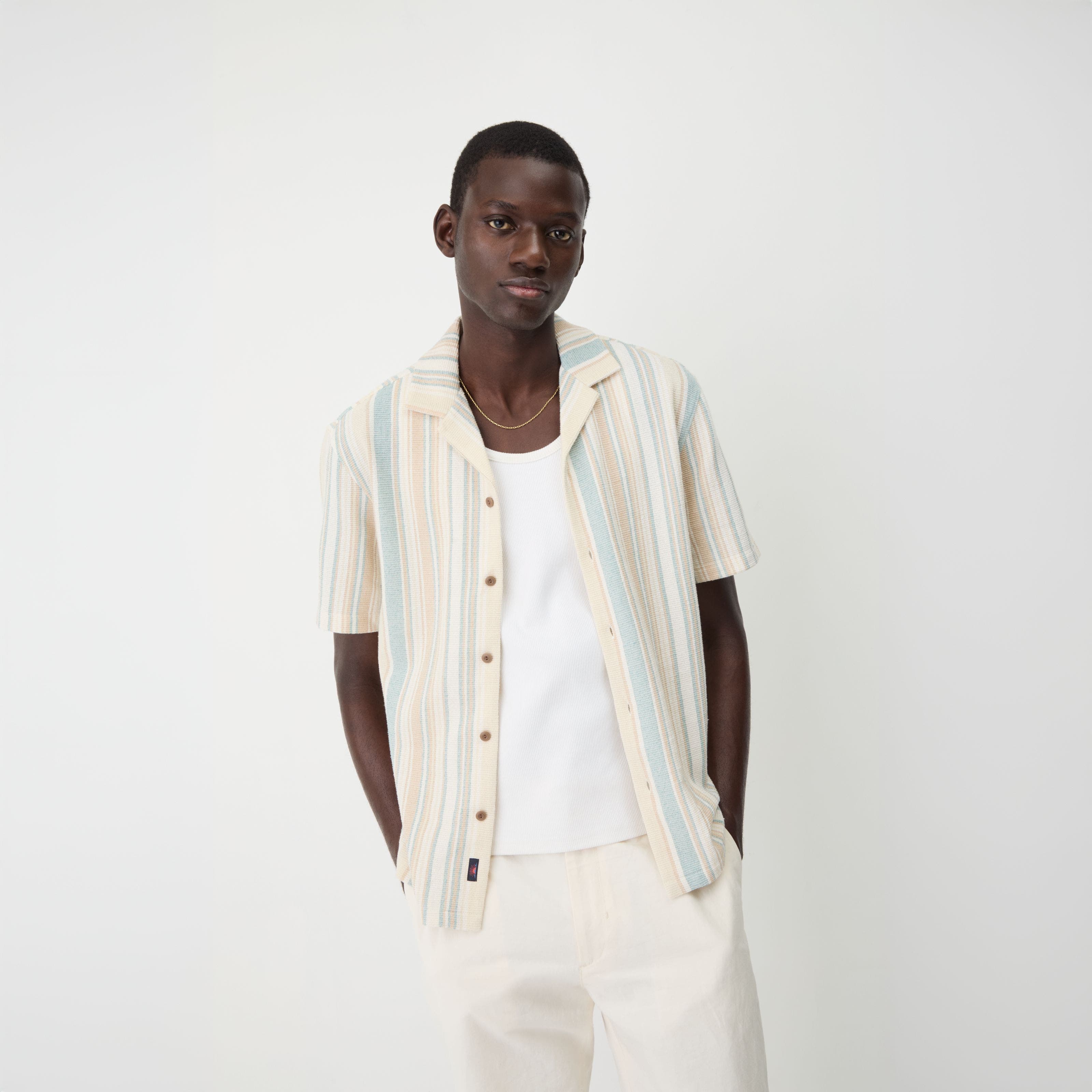A man wearing a striped short-sleeve button-up shirt with a white T-shirt.