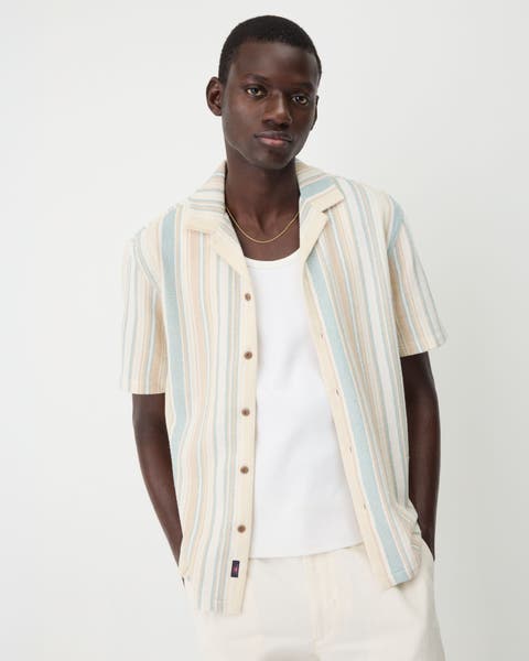 A man wearing a striped short-sleeve button-up shirt with a white T-shirt.