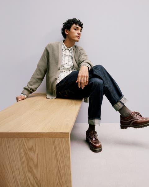 Man wearing a cardigan, flannel shirt, jeans and oxford shoes.