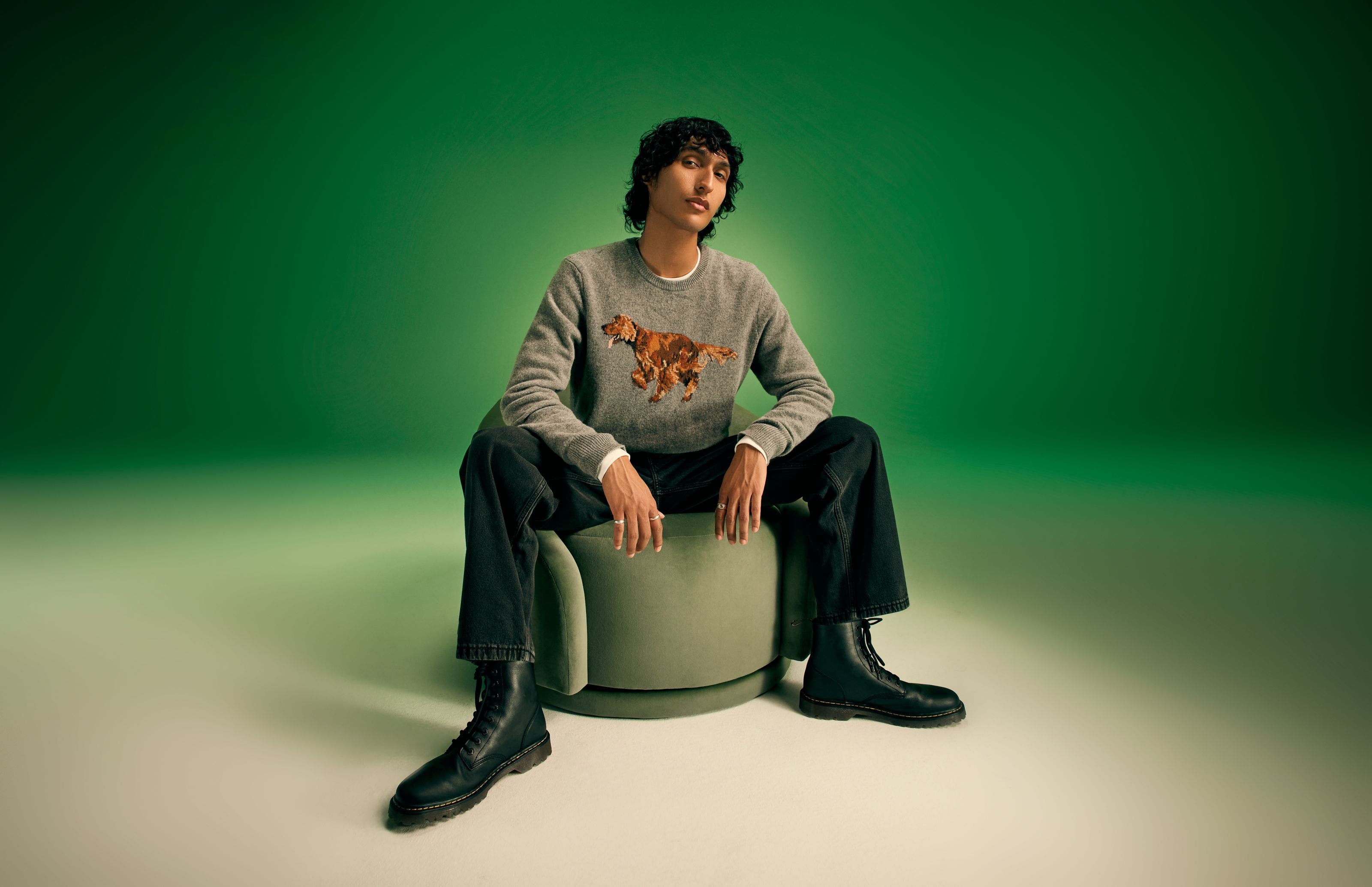 A man wearing a grey sweater with jeans and black boots.