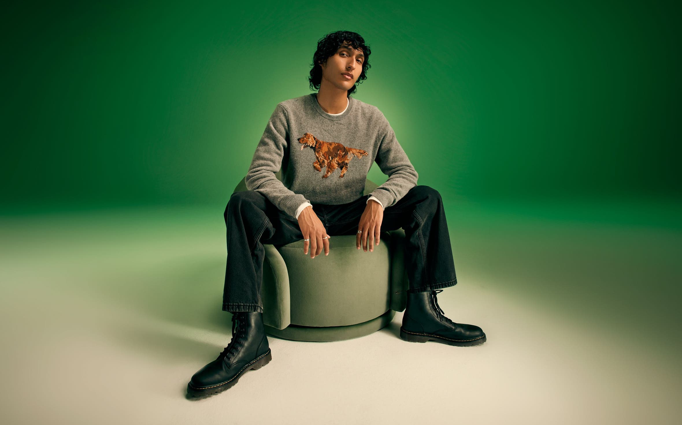A man wearing a grey sweater with jeans and black boots.
