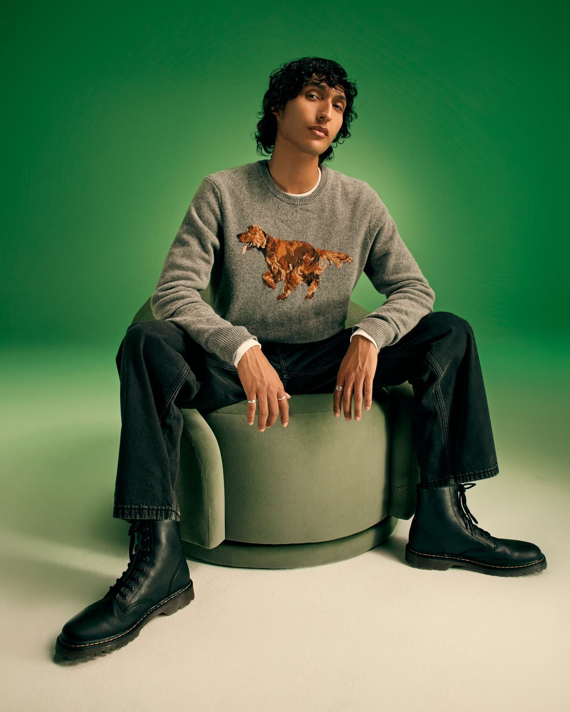 A man wearing a grey sweater with jeans and black boots.