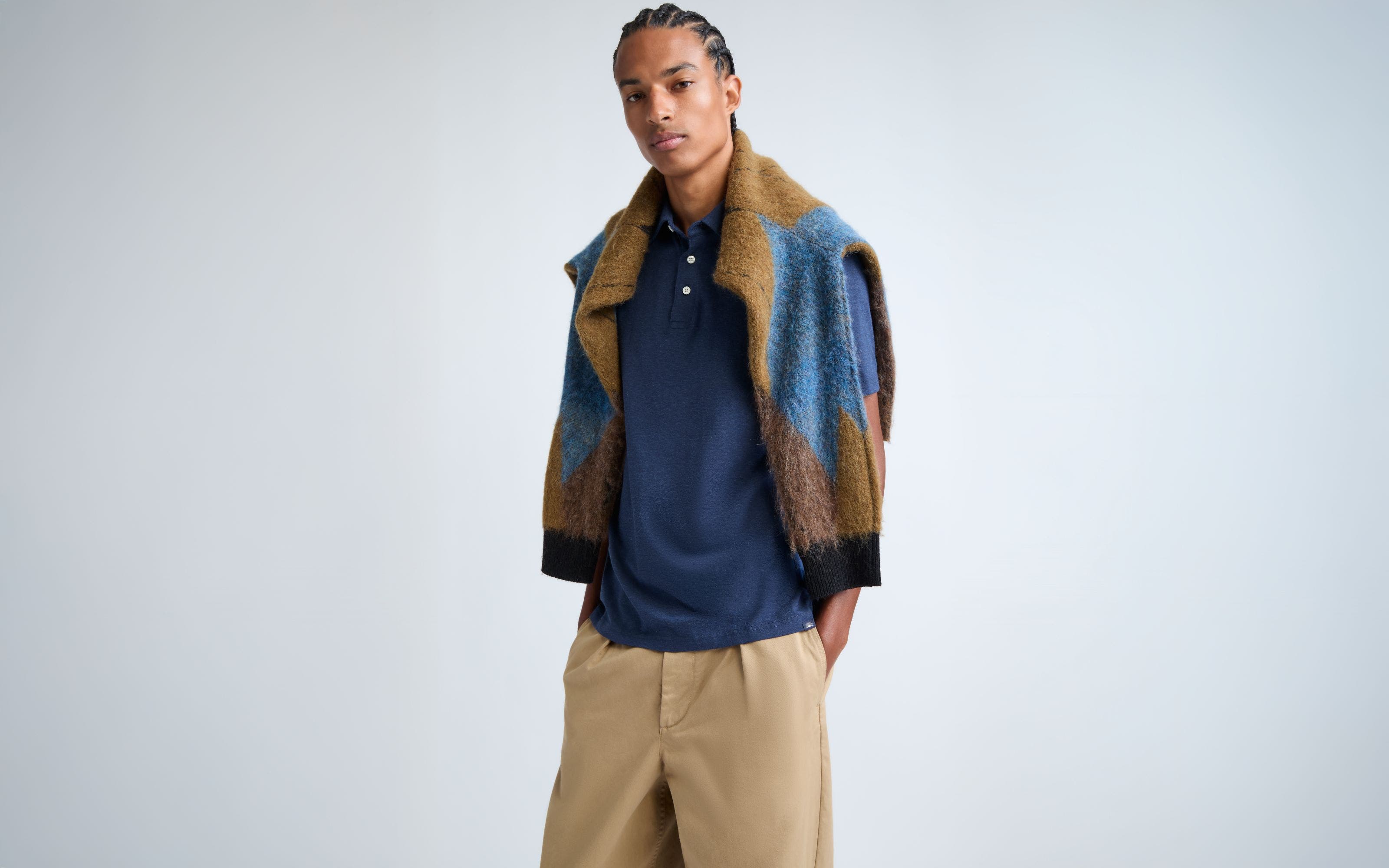 A man wearing a navy polo and khaki pants with a patterned sweater draped over his shoulders.