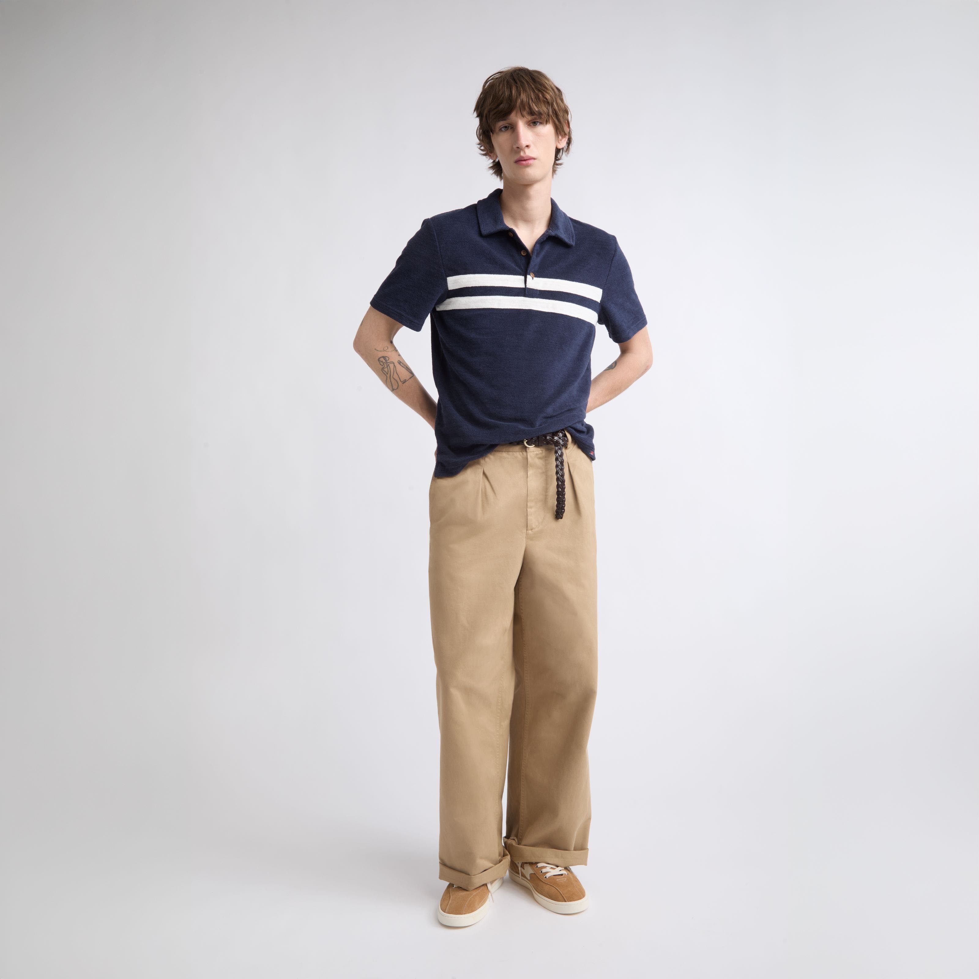 A man wearing a striped navy polo with khaki pants and low-top sneakers.