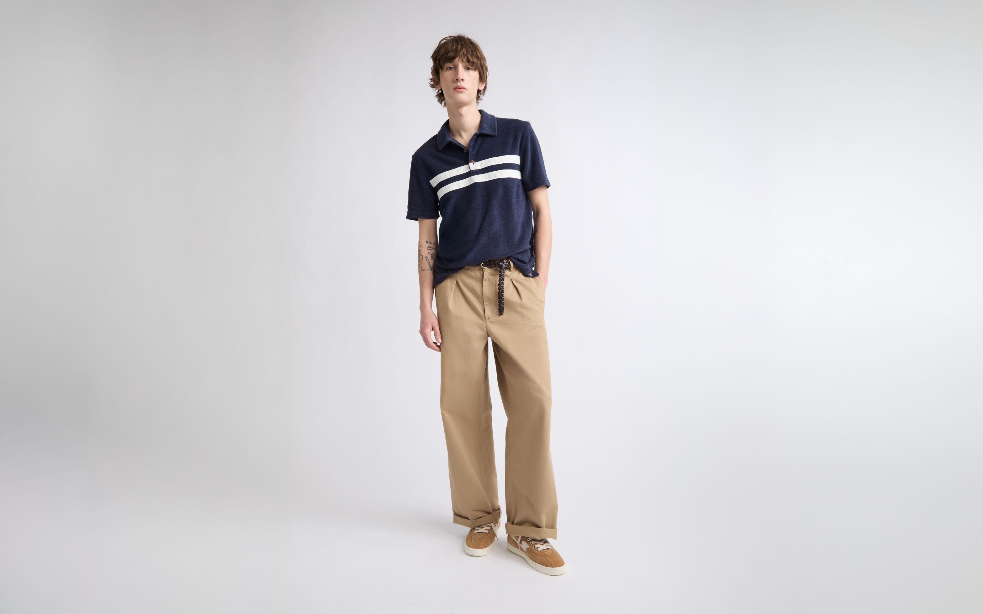 A man wearing khaki pants with a striped navy polo and low-top sneakers.