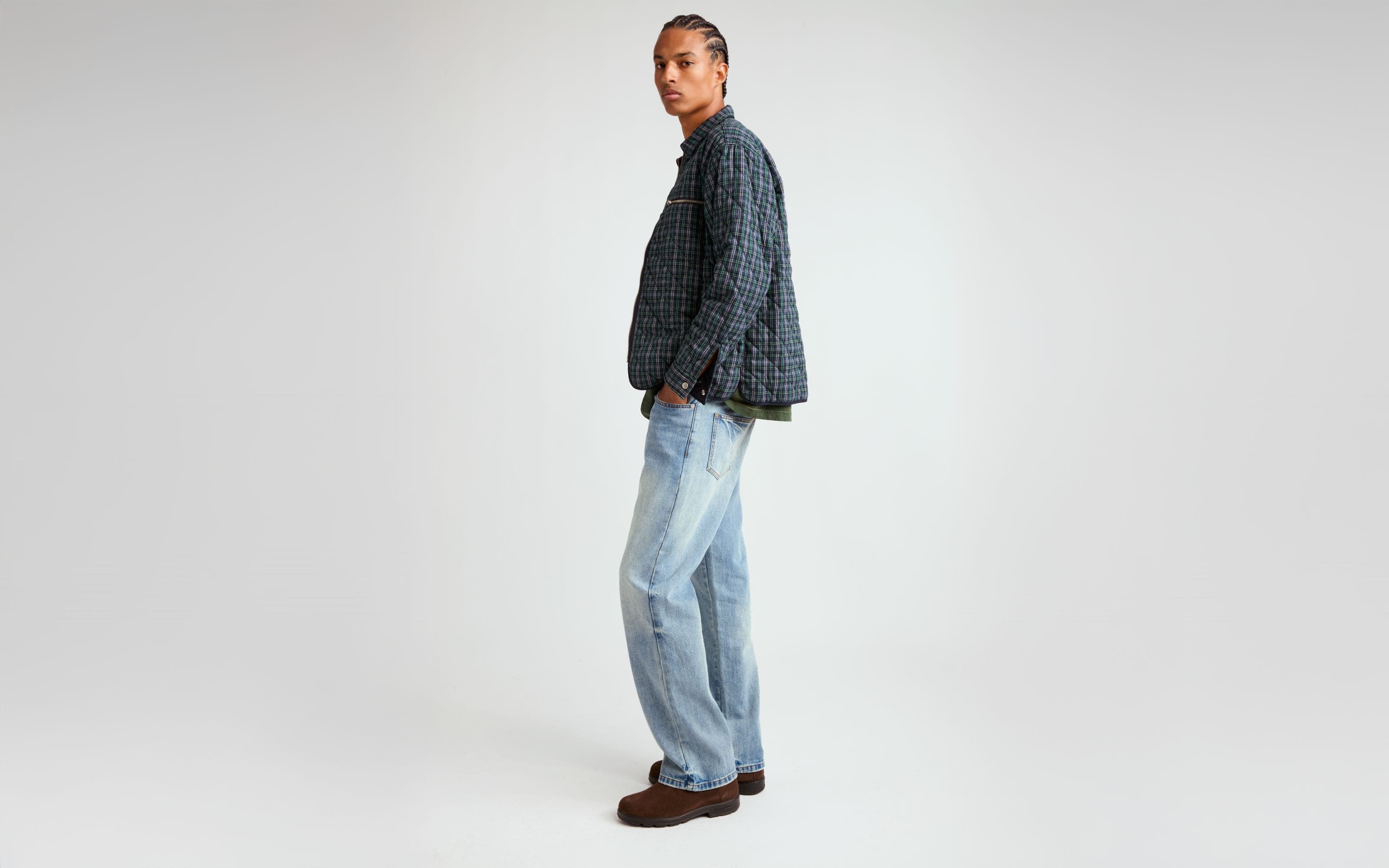 A man wearing a quilted jacket and light blue jeans.