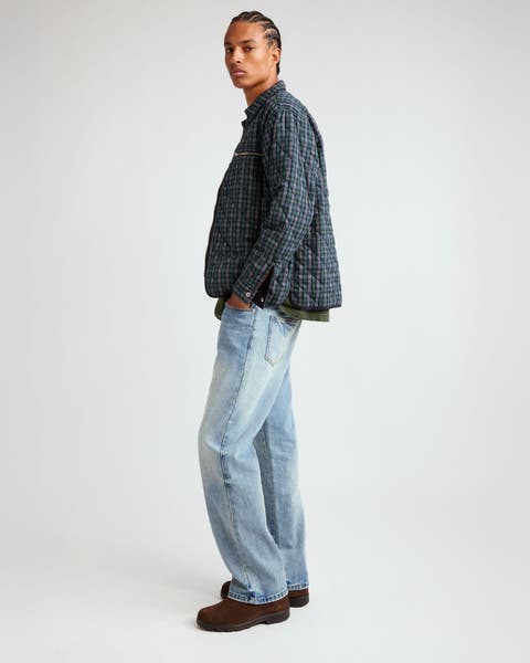 A man wearing a quilted jacket and light blue jeans.