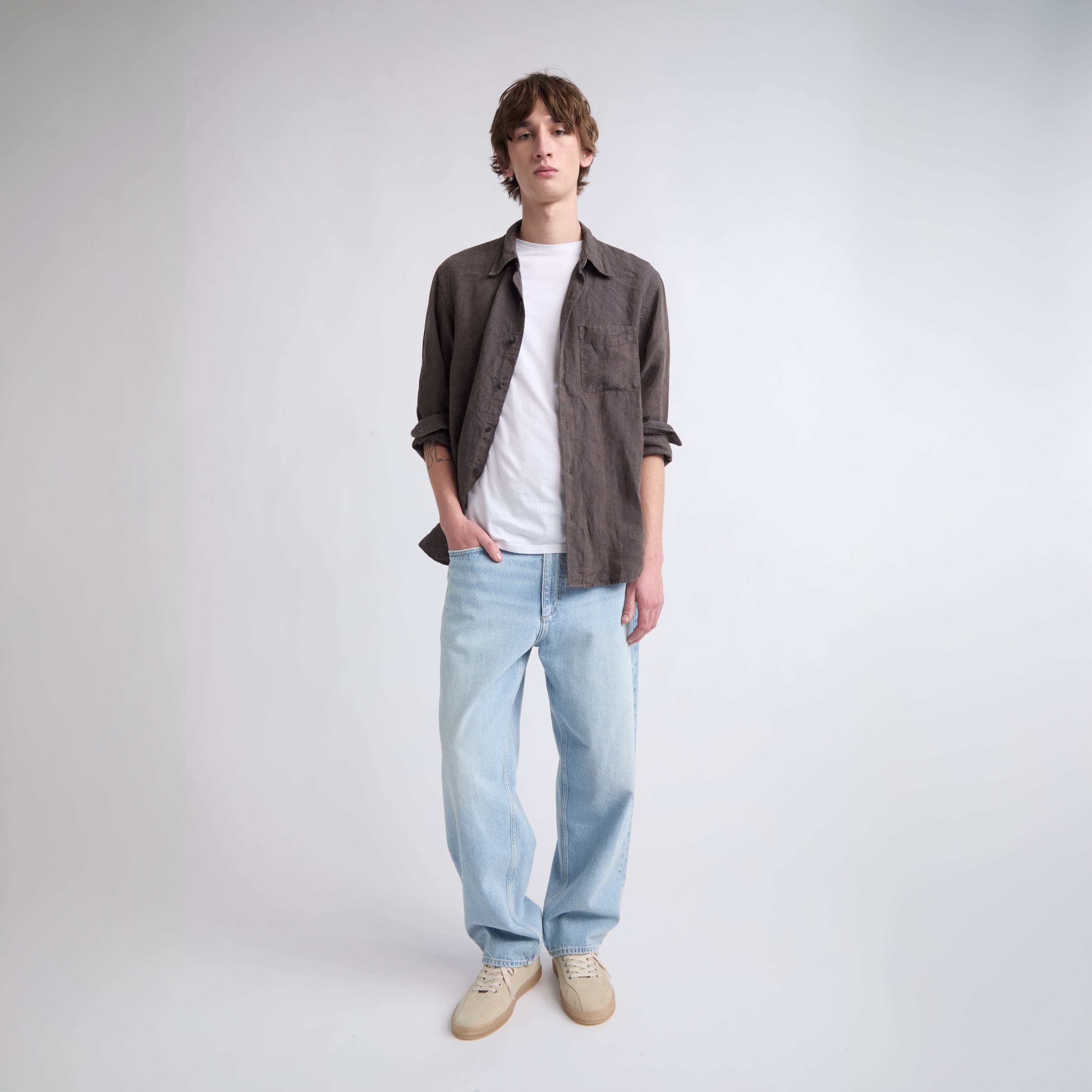 A man wearing light-blue jeans with a white T-shirt and button-up shirt. 