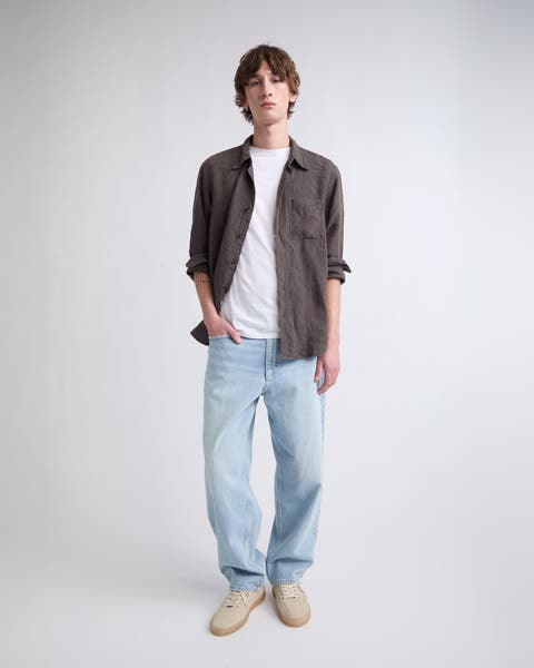 A man wearing light-blue jeans with a white T-shirt and button-up shirt. 