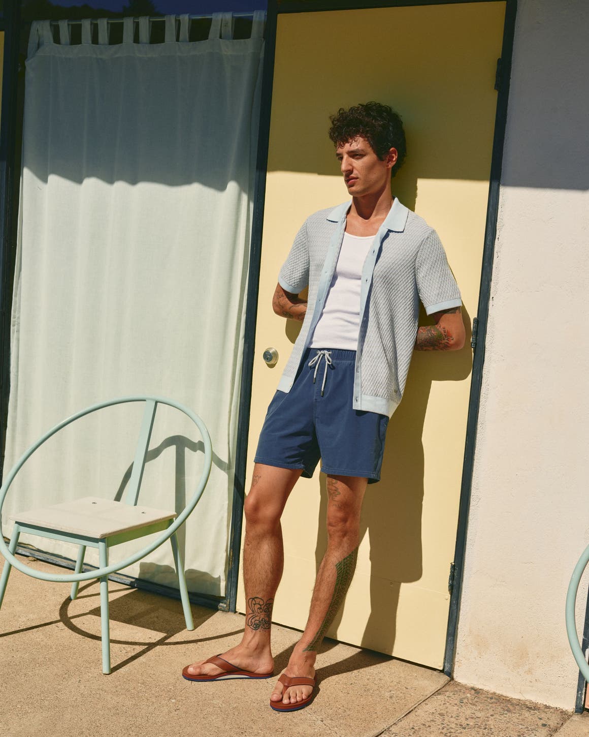 Man wearing a knitted camp shirt, white tank top and blue shorts.