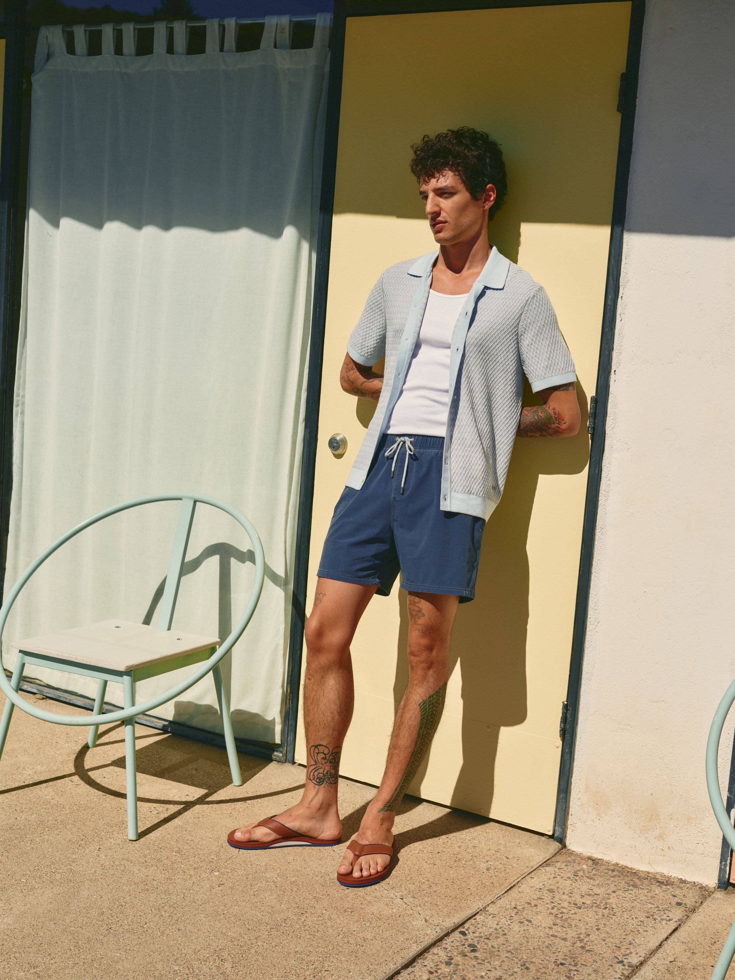 Man wearing a light cardigan over a tank with swim shorts.