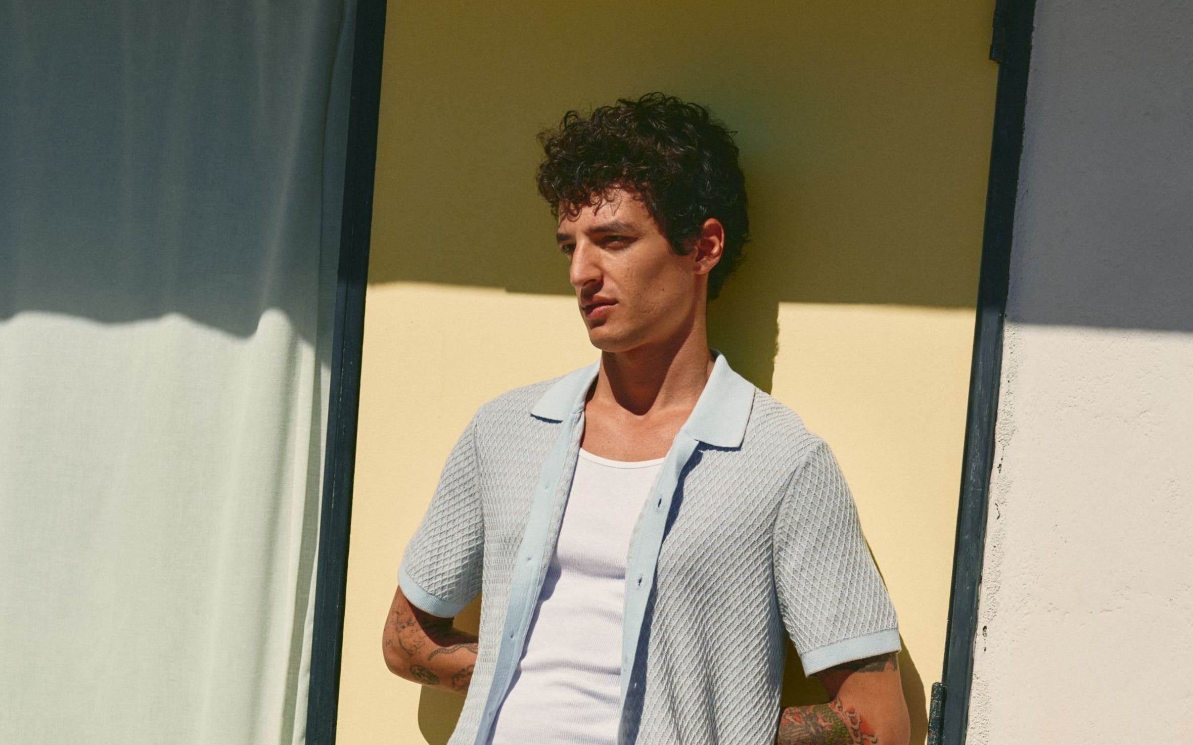Man wearing a light cardigan over a tank with swim shorts.