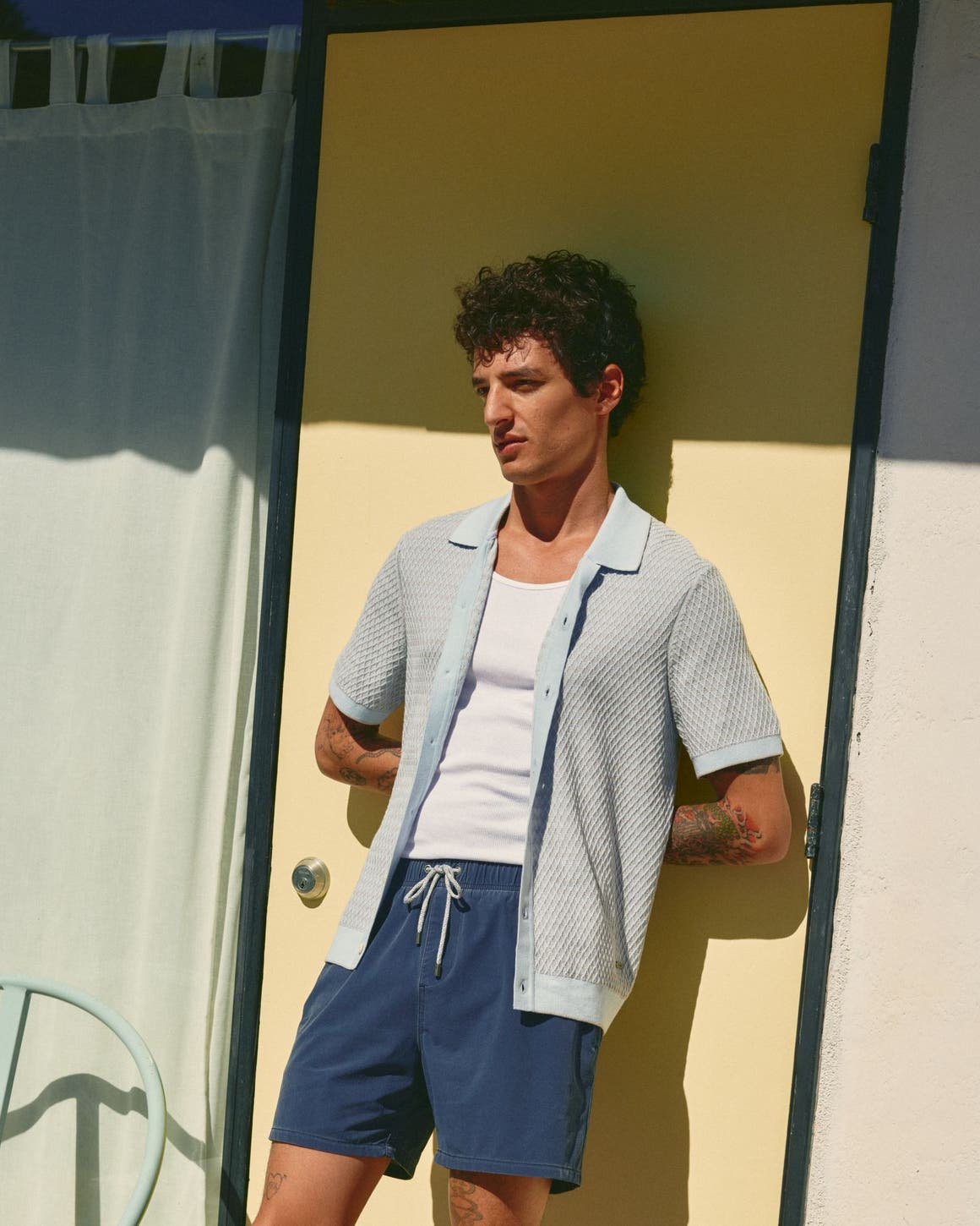 Man wearing a light cardigan over a tank with swim shorts.