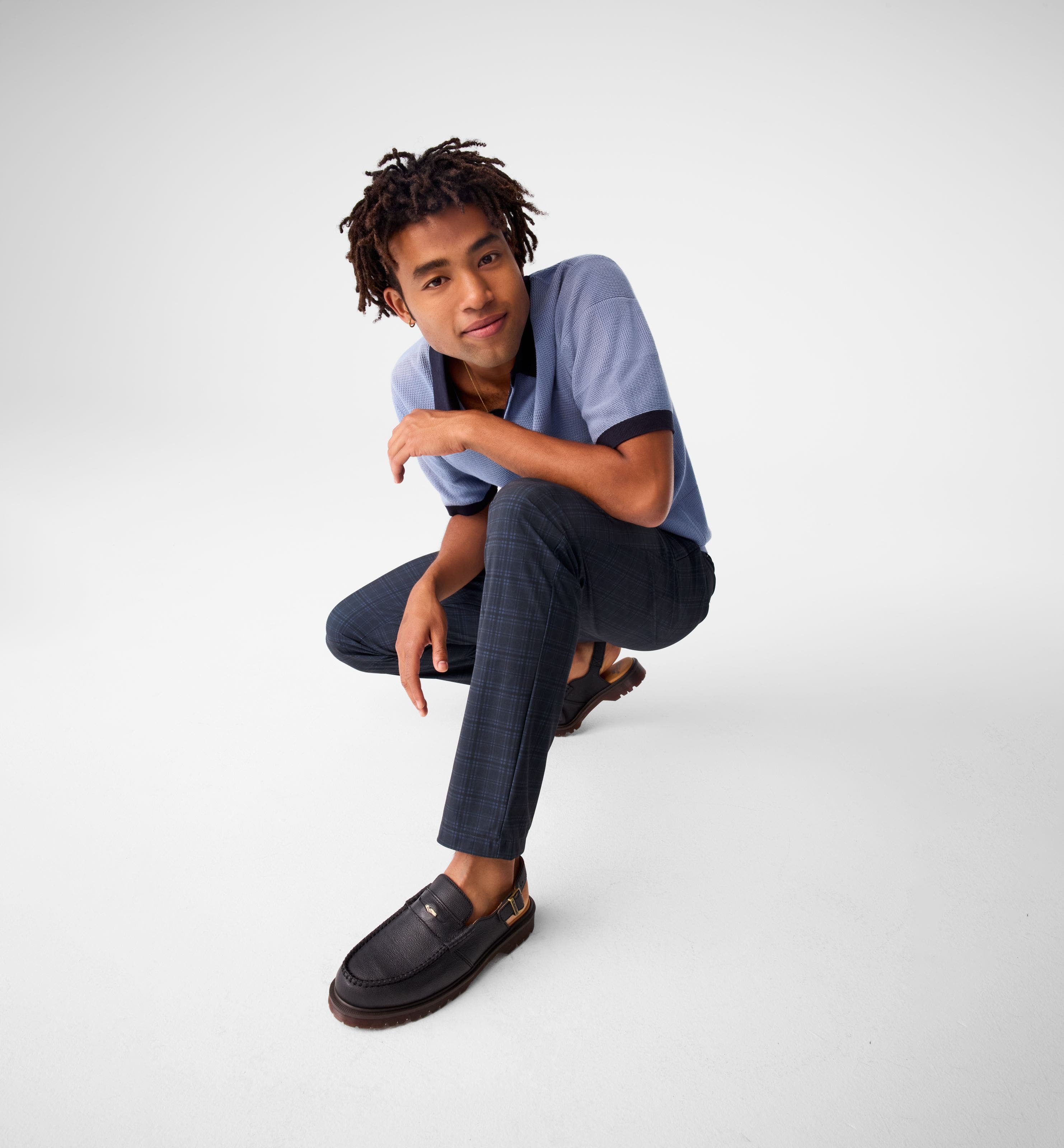 A man wearing a blue polo with navy plaid pants and loafers. 