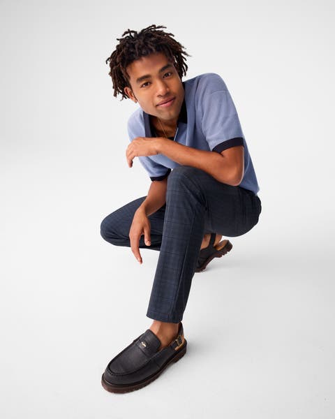 A man wearing a blue polo with navy plaid pants and loafers.