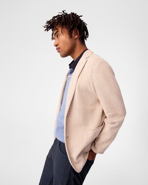 A man wearing a cream sport coat, blue shirt and plaid pants.