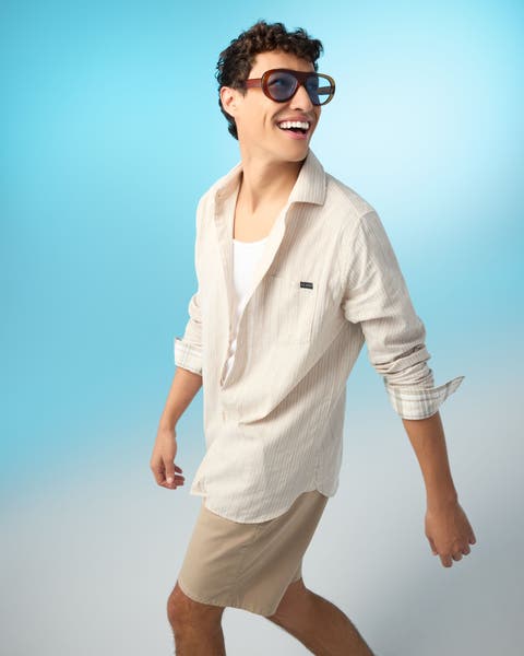 A man wearing a white tank, a striped cream shirt and tan shorts.