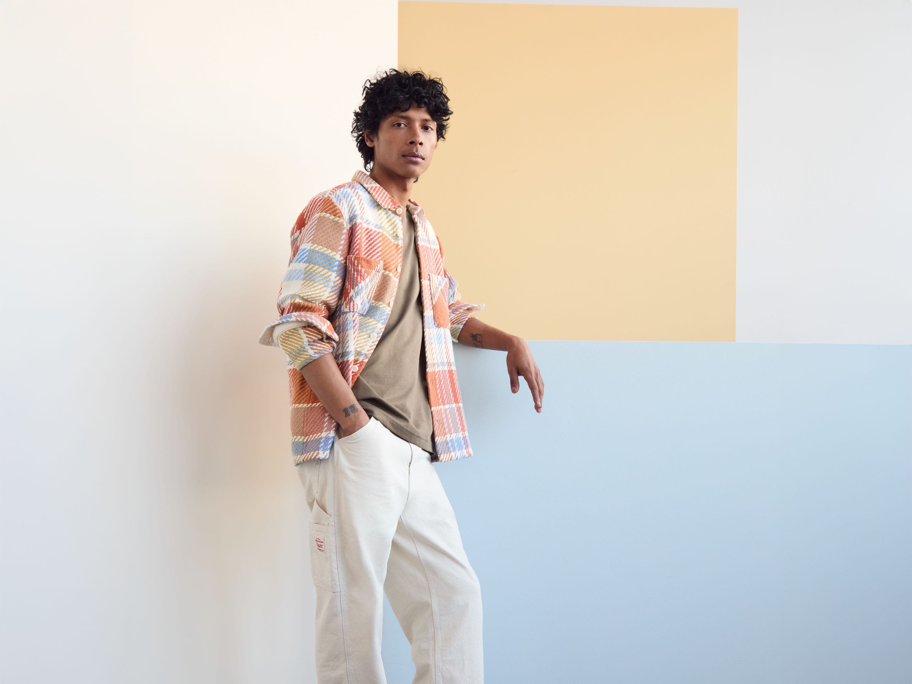 A man in a colorful shirt jacket with neutral tee and pants.