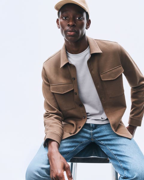 Man wearing a shirt jacket, T-shirt, jeans and cap.