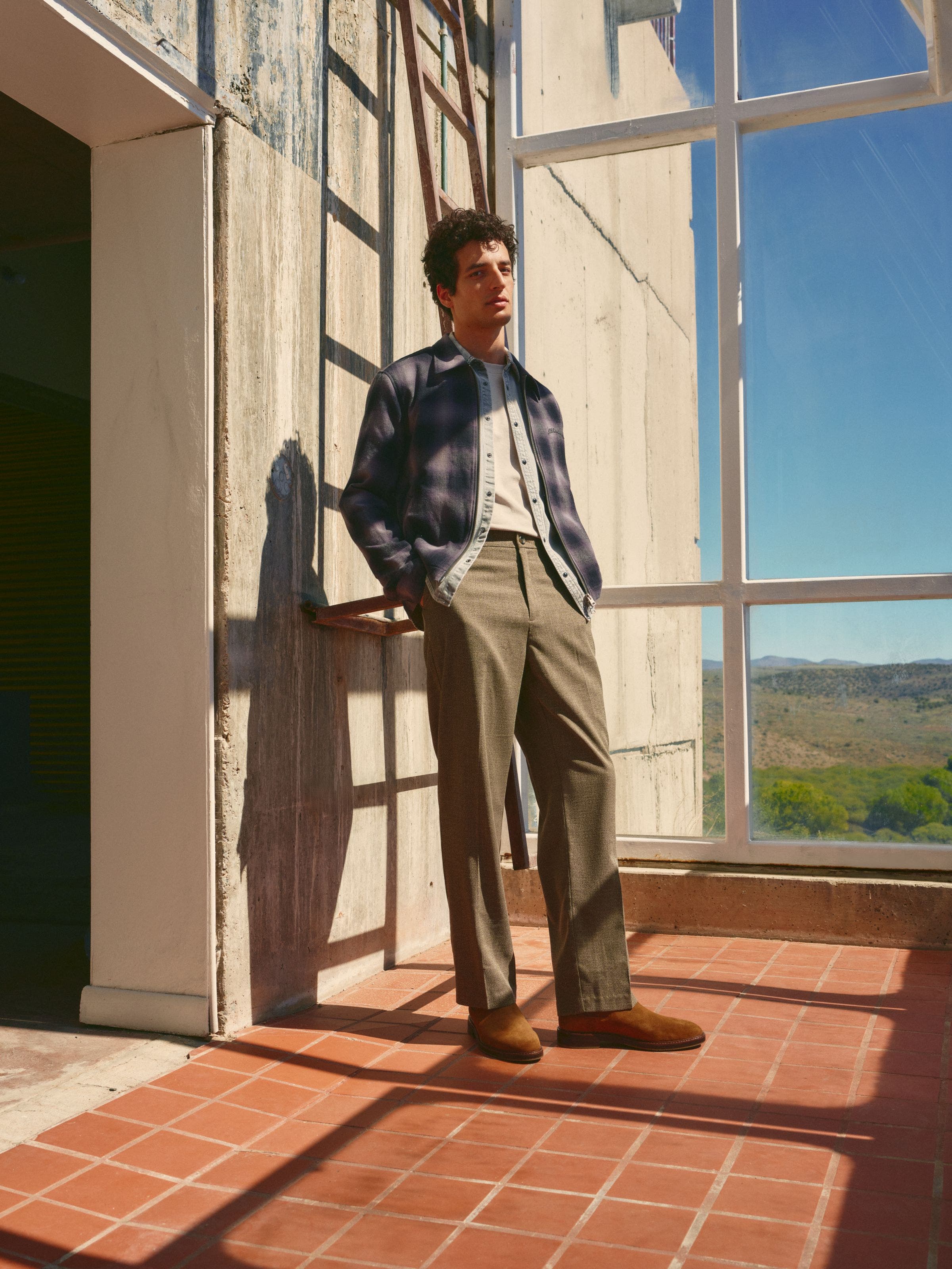 Man wearing brown pants and a flannel shirt over a denim shirt and T-shirt.
