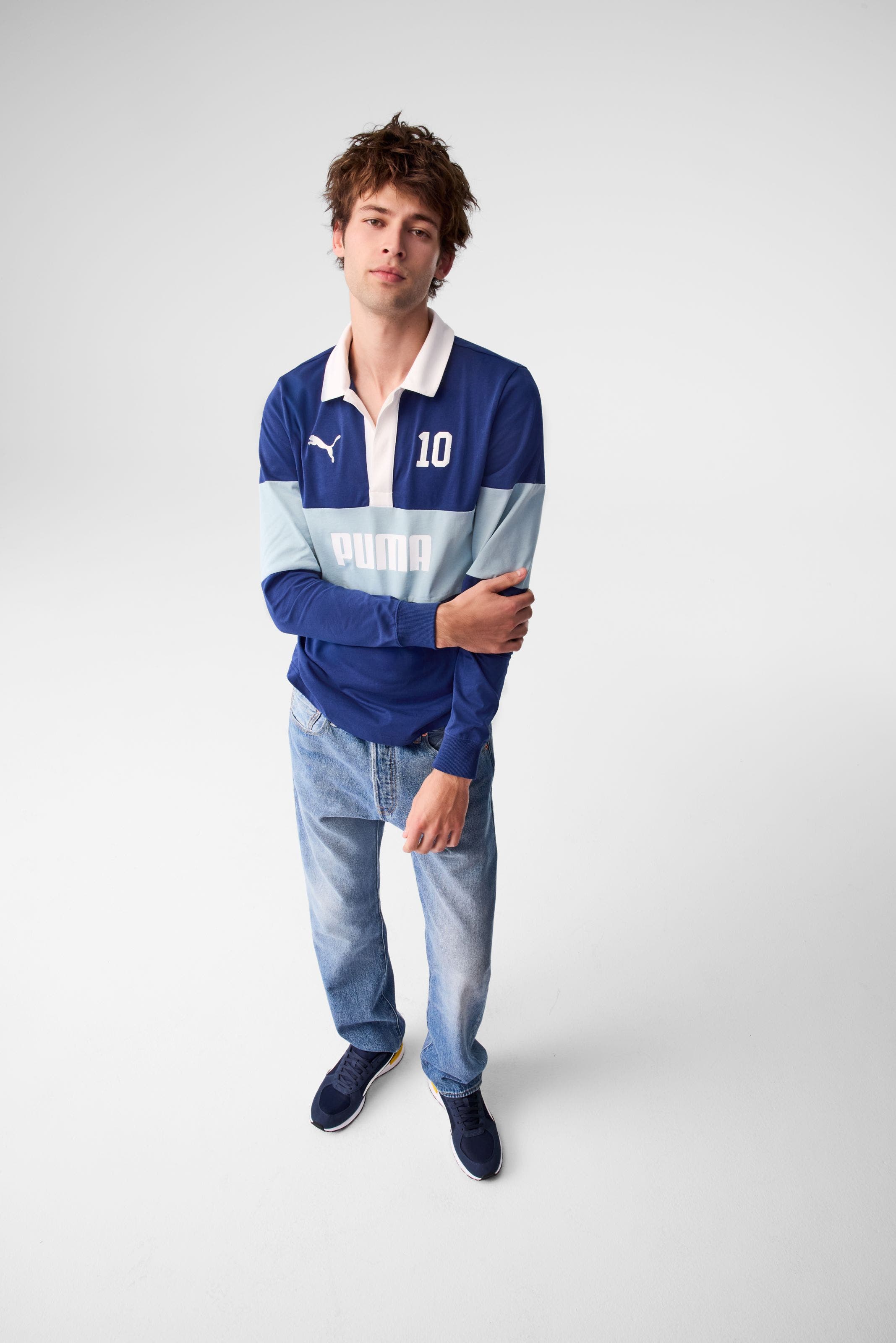 A man wearing a blue polo shirt, jeans and navy sneakers.