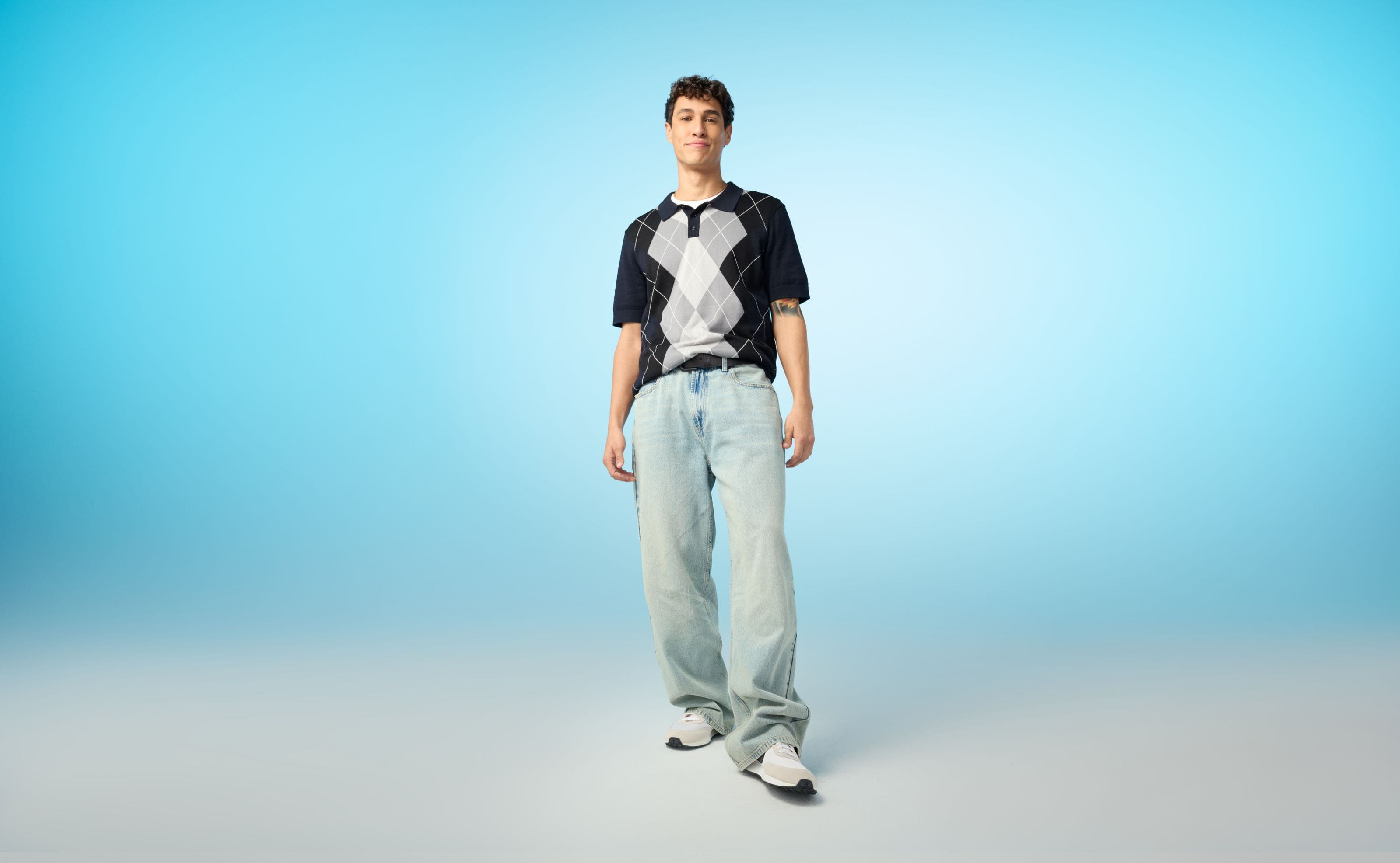 A man wearing a knit argyle and light-wash blue jeans.