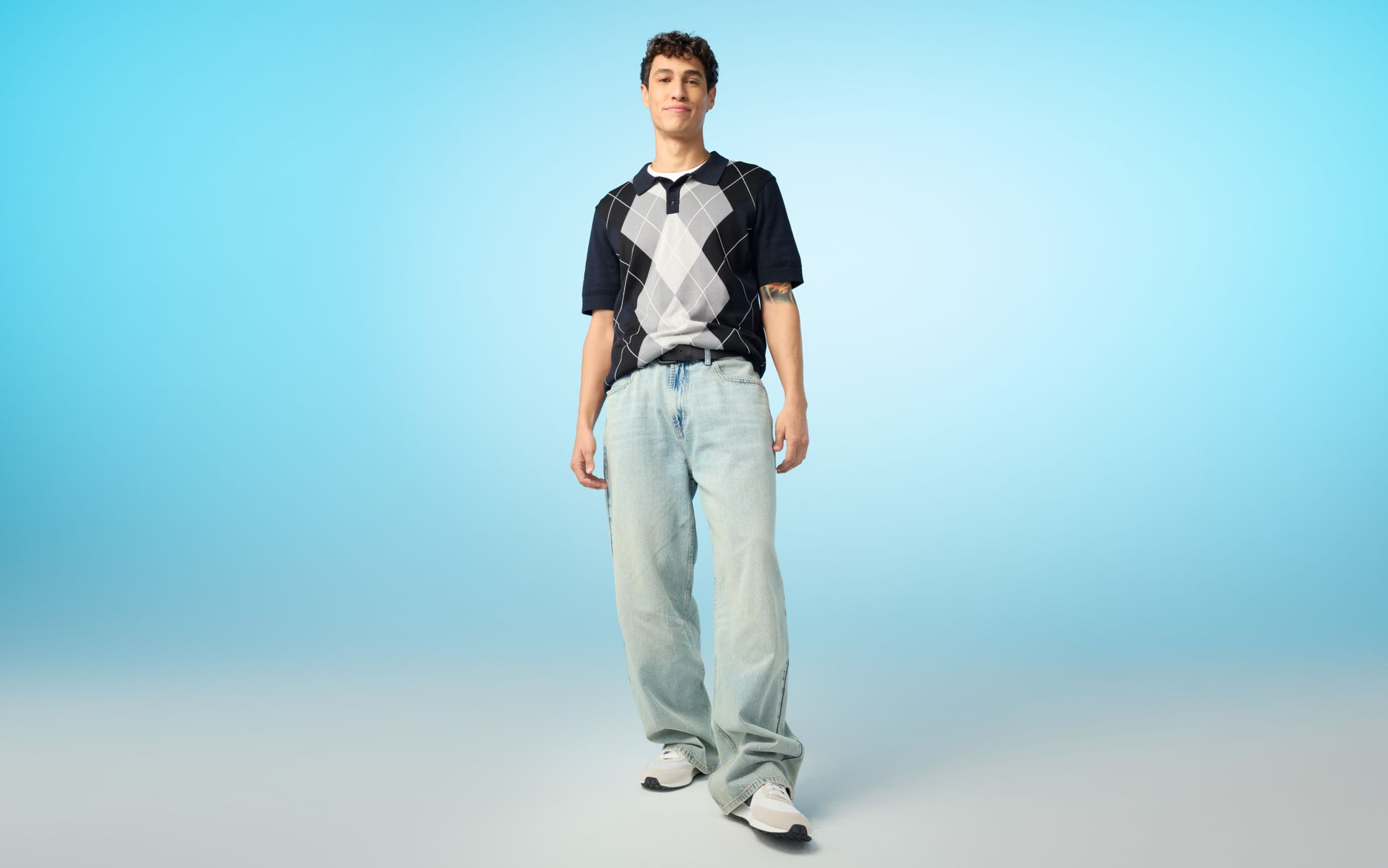 A man wearing a knit argyle and light-wash blue jeans.