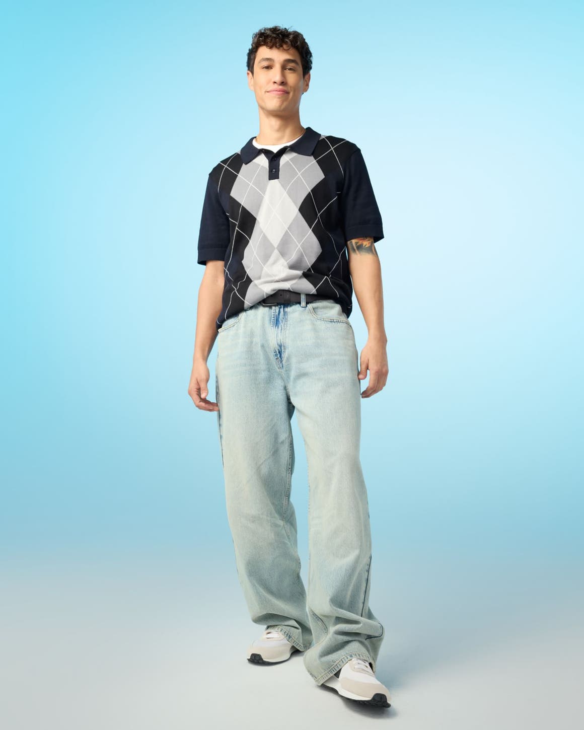 A man wearing a knit argyle and light-wash blue jeans.