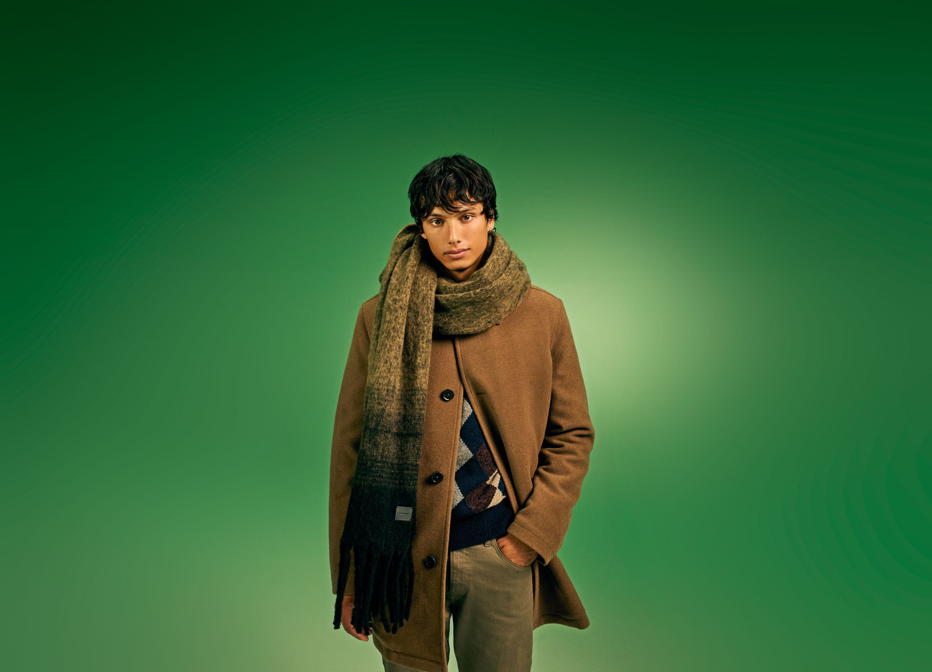 A man wearing a scarf with a coat, sweater and pants.