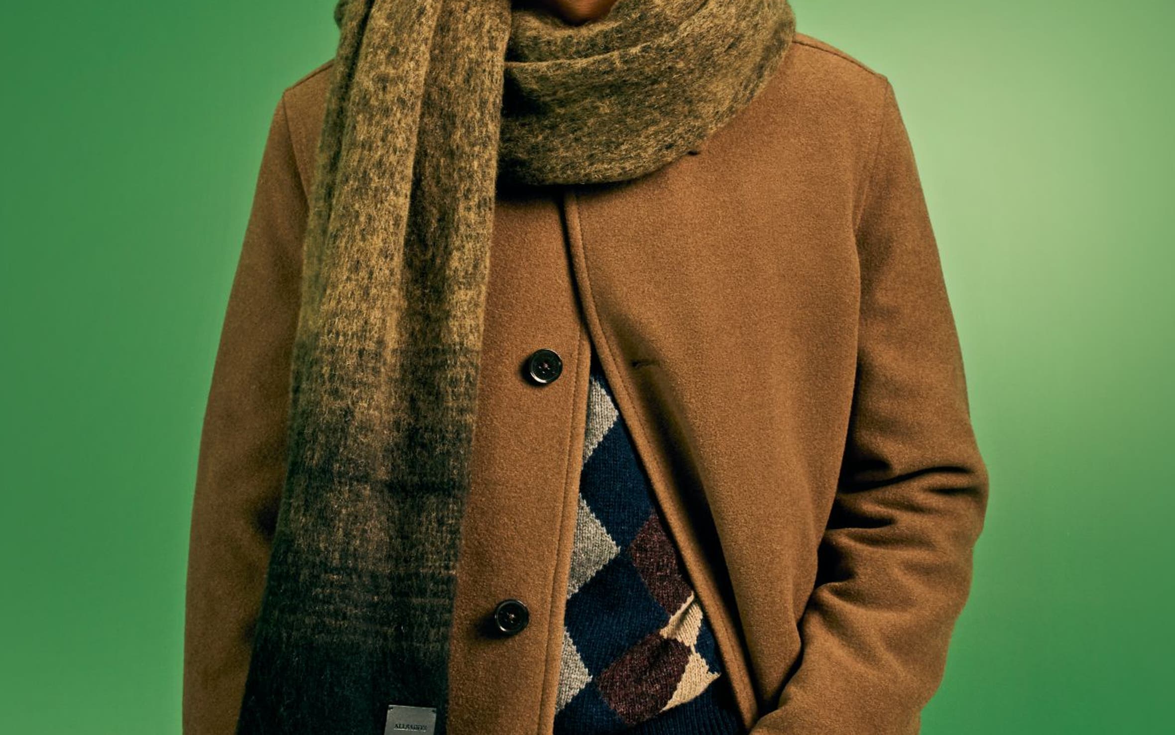 A man wearing a scarf with a coat, sweater and pants.
