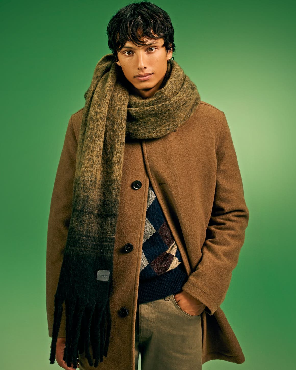 A man wearing a scarf with a coat, sweater and pants.